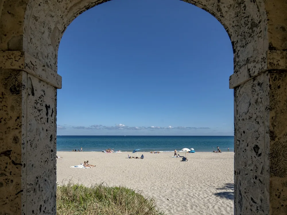 Palm Beach sand and ocean framed by a stone clock-tower arch — illustrative journey photograph